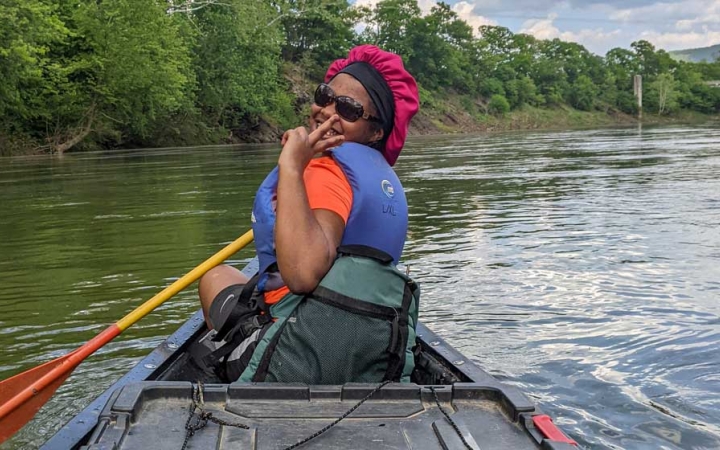 a student smiles and gives a peace sign while sitting in a canoe